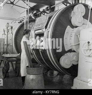 Années 1950, historique, les travailleurs laitiers en blouse blanche contrôle du beurre qui a été faite à l'intérieur d'une grande mécanique de type barillet baratte, en Irlande. Banque D'Images