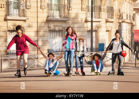 Le patin à roues alignées et la planche à roulettes adolescents multiethnique tenant la main le long du trottoir Banque D'Images