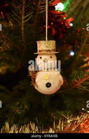 Libre d'un bonhomme de neige décoration d'arbre de Noël accroché sur une épinette de Norvège, entouré par les aiguilles de pin et encadrées de guirlandes et de lumières de la bougie. Banque D'Images