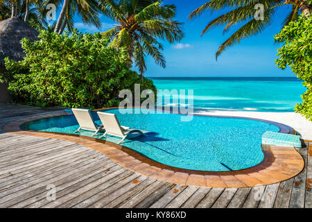 Secteur piscine en front de mer avec des chaises submergées dans un resort de luxe aux Maldives, l'Océan Indien Banque D'Images