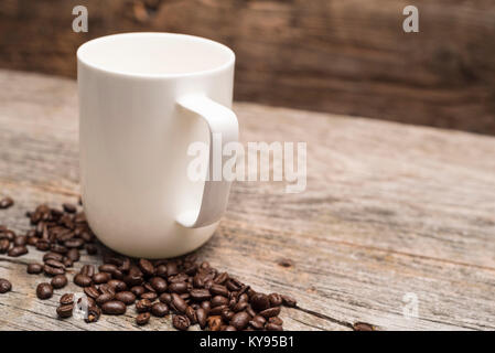 Une grande tasse à café blanc entouré de grains de café torréfiés tourné contre brun rustique barn wood background prêts à verser Banque D'Images