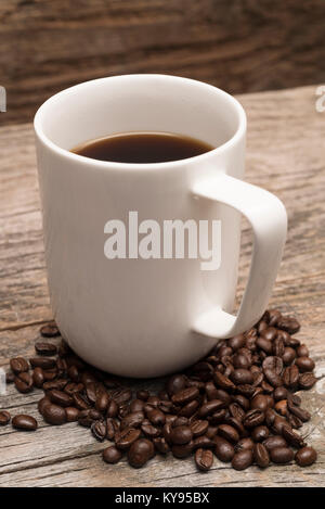 Dans une grande tasse de café blanc entouré de grains de café torréfiés tourné contre brun rustique barn wood background Banque D'Images