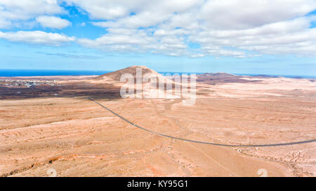 Vue aérienne de la vallée du désert avec un pic volcanique près de mer, traversée de la route de l'espace ouvert, Fuerteventura, Îles Canaries, Espagne . Banque D'Images
