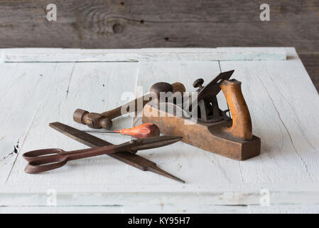 Collection de meubles anciens, vintage outils, y compris hammer, poinçon, fichier, d'une cisaille et la cale en bois avion, contre le bois peint blanc patiné ba Banque D'Images