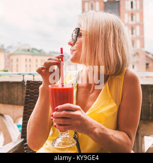 Une femme à boire un cocktail sur la terrasse d'un café en face de l'église St Mary à Cracovie. La Pologne. Banque D'Images