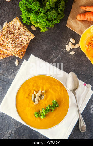 Bol de citrouille rôties et crème de carottes soupe de persil et de graines de citrouille sur la table en pierre sombre servi avec des ingrédients. Selective focus, Copier sp Banque D'Images