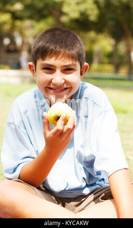 Teenage Boy eating green apple avec l'expression du visage Banque D'Images