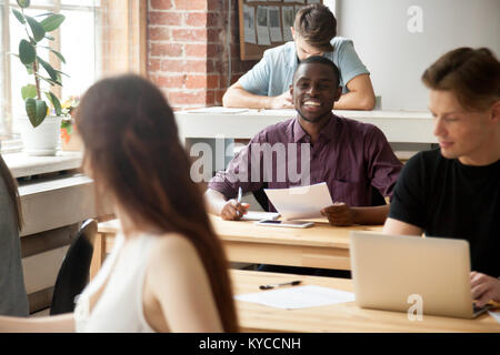 Cheerful africains-américains nouvel employé parlant à collègue multi-ethnique en co-working space, friendly smiling man holding documents demande que Banque D'Images