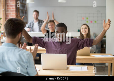 Employé de l'Afrique de l'enthousiaste à gagner en ligne sensibilisation mains looking at laptop, bureau coworking applaudir l'équipe collègue noir féliciter avec parvenir Banque D'Images