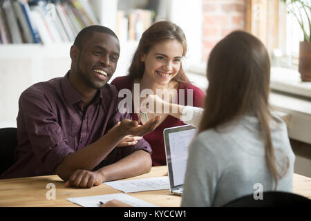 Heureux couple multiracial pour obtenir de nouvelles accueil de realtor, excité les jeunes clients l'achat vente maison concept, divers acheteurs famille purcha Banque D'Images