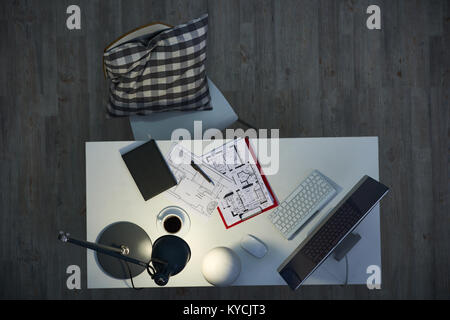 Intérieur de dim design studio : Oreiller confortable allongé sur une chaise, plans d'étage, Bloc-notes et l'ordinateur moderne situé sur la lampe de bureau éclairé par Banque D'Images