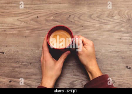 Vue depuis le haut de deux mains tenant une tasse rouge remplie de café sur une table en bois Banque D'Images