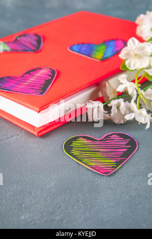 Coeur noir et rose sur un livre dans un couvercle rouge et de fleurs sur un fond de béton gris. Le concept de la Saint-Valentin. Un symbole de l'amour Banque D'Images