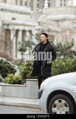 L'homme élégant wolk dans la rue. Froid d'hiver tenue. Veste avec Big White sneakers. Fond Blured street. Modèle photo Profecional. Banque D'Images