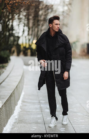 L'homme élégant wolk dans la rue. Froid d'hiver tenue. Veste avec Big White sneakers. Fond Blured street. Modèle photo Profecional. Banque D'Images