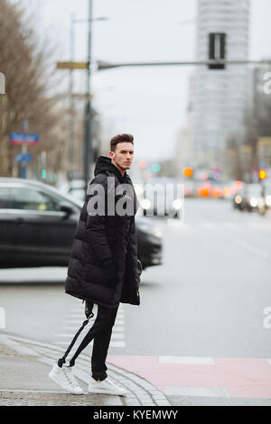 L'homme élégant wolk dans la rue. Froid d'hiver tenue. Veste avec Big White sneakers. Fond Blured street. Modèle photo Profecional. Banque D'Images