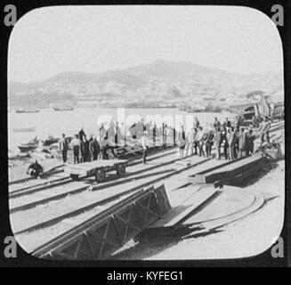 Vladivostok, Russie, montrant les travailleurs des chemins de fer à quai avec la ville et le port en arrière-plan, illustrant l'activité industrielle du début du XXe siècle. Banque D'Images