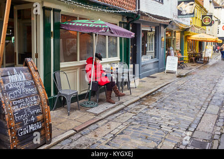 Tourisme âgés femme assise à l'extérieur d'un pub et un café lecture à Mercery Lane, Canterbury Banque D'Images