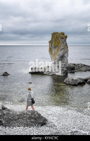 Gotland, Faro, en Suède, une femme marche seule sur une plage de rochers à proximité d'un rauk, un énorme rocher dans l'eau de la mer Baltique. La verticale. Banque D'Images