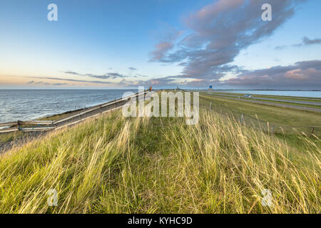 Afsluitdijk digue néerlandaise avec des clôtures d'autoroute et piste cyclable pendant le coucher du soleil avec ciel assombri Banque D'Images