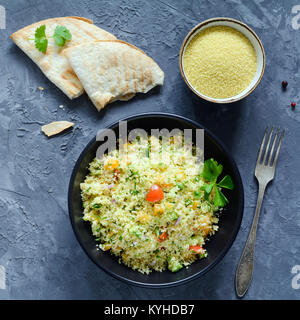 Taboulé salade et du pain plat sur fond de béton. Des Libanais, des arabes. Salade de couscous végétalien sain en noir bol. Vue de dessus de table carré, cr Banque D'Images