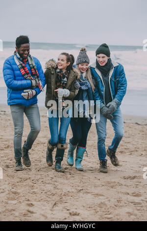 Un groupe d'amis parler et rire tout en marchant le long d'une plage d'hiver. Banque D'Images