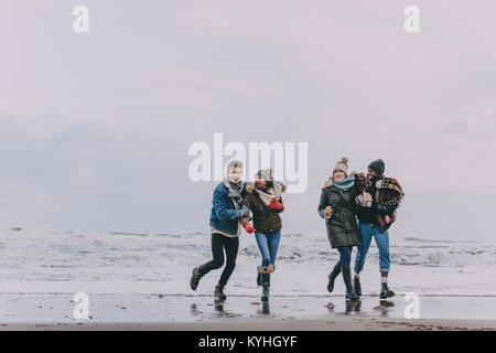 Un groupe d'amis qui rient tout en explorant une plage d'hiver. Banque D'Images