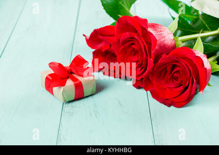 Roses rouges et un petit cadeau fort avec un ruban rouge sur une table en bois aquamarine Banque D'Images