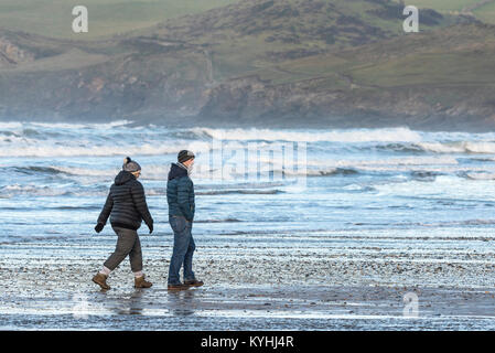 Polzeath - un couple de personnes bénéficiant d'une promenade sur la plage de Polzeath sur la côte nord des Cornouailles. Banque D'Images