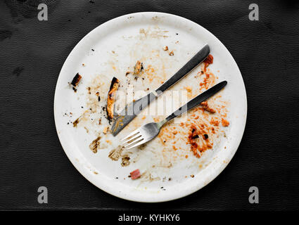 D'un grand angle de vue d'une plaque en céramique blanche avec les restes d'une pizza, sur une surface en similicuir noir Banque D'Images