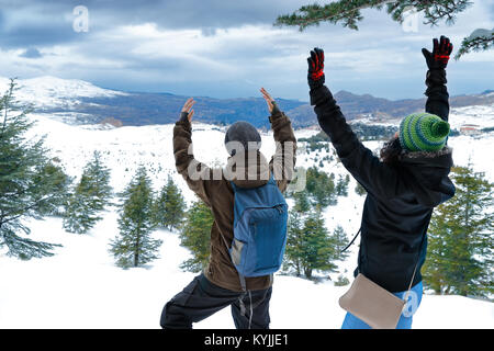 Deux happy friends enjoying vacances d'hiver, l'homme et la femme debout avec les mains jusqu'à la montagne, en profitant du paysage recouvert de neige, ayant Banque D'Images