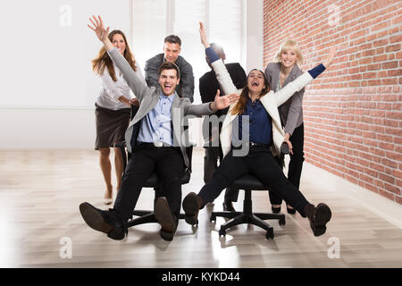 Smiling Businesspeople jouer ensemble avec fauteuil pivotant dans le bureau Banque D'Images