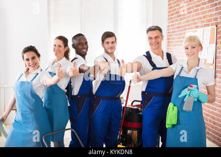 Professionnels Divers concierges dans le bureau avec des équipements de nettoyage Showing Thumb Up Sign Banque D'Images