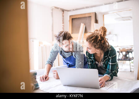 Jeune couple avec un ordinateur portable dans l'atelier de charpentier. Banque D'Images