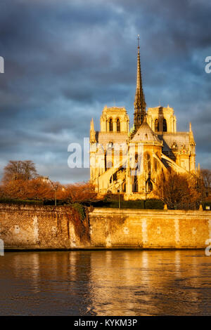 Paris, France Notre Dame de rougeoyer en golden sunrise aube lumière, brillant contre des nuages sombres. Les réflexions dans le fleuve ci-dessous. L'image spectaculaire. Banque D'Images