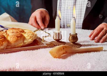 La Challah ou Hala est un sabbat juif traditionnel sweet pain frais. Mains des hommes garder pain et deux bougies en cire dans les chandeliers. Banque D'Images