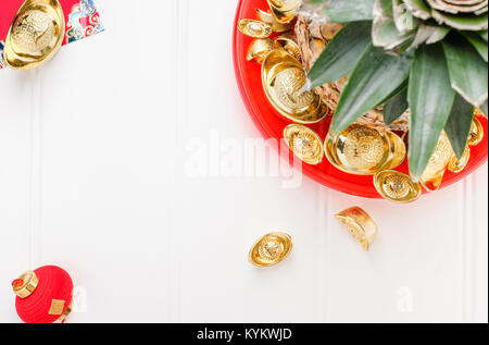 Le nouvel an chinois ang pow concept.Vue de dessus de l'ananas avec groupe de lingots d'or dans le bac rouge sur table en bois blanc.sur moyenne des lingots riches. Banque D'Images