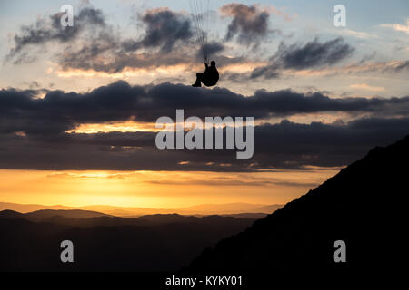 Beau coup d'une silhouette parapente voler au-dessus de Monte Cucco (Ombrie, Italie) avec le coucher du soleil sur l'arrière-plan, avec de belles couleurs et les tons sombres Banque D'Images