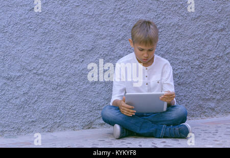 Enfant avec ordinateur tablette assis sur le sol à l'extérieur Banque D'Images