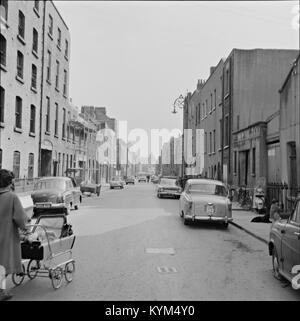 Une photographie historique de Queen Street à Dublin, montrant diverses voitures, dont une Austin Cambridge et une Ford Anglia, garées dans la rue. La scène capture la vie quotidienne à Dublin avec une architecture historique et des véhicules du passé. Banque D'Images