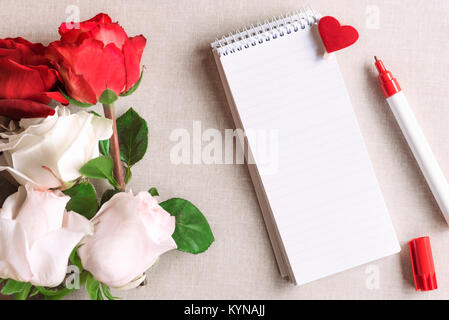 Ouvrez Carnet à spirales avec des rayures et un clip en bois avec coeur rouge épinglée sur elle et un bouquet de roses blanches et rouges, sur un fond de tissu vintage. Banque D'Images
