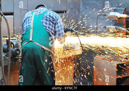 Des travailleurs dans une fonderie moulages grind avec une meuleuse - milieu de l'industrie lourde Banque D'Images
