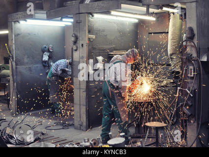 Des travailleurs dans une fonderie moulages grind avec une meuleuse - milieu de l'industrie lourde Banque D'Images