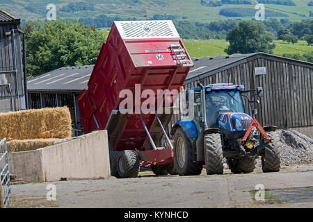 New Holland tracteur à quatre roues motrices avec une remorque d'ensilage Marshall le déchargement d'une cargaison de l'ensilage dans une cour de ferme au moment de la récolte, Cumbria, Royaume-Uni. Banque D'Images