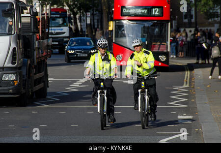 Londres, Angleterre, Royaume-Uni. Deux femmes de la Police métropolitaine offre sur les bicyclettes en avant d'un bus à impériale rouge Banque D'Images