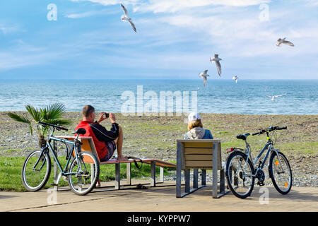 Après le week-end de repos en vélo - un couple s'asseoir sur des chaises longues et profiter d'une vue magnifique sur la mer et les mouettes, ce qui en photo sur le smartphone. Banque D'Images