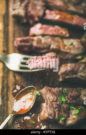 Grillades de bœuf saignante ribeye coupé en morceaux sur la planche de bois rustique avec sauce chutney de mangue, portrait, close-up Banque D'Images