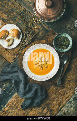 Télévision à jeter de potage à la citrouille de réchauffement de l'automne avec des croûtons et des graines à bord plus rustique en arrière-plan, Vue de dessus, la composition verticale. Légumes d'automne Banque D'Images