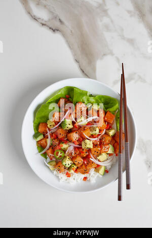 Poke saumon photographié d'au-dessus dans un bol blanc sur une surface en marbre blanc. Banque D'Images