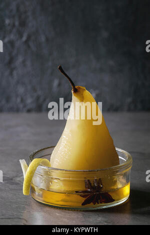 Dessert traditionnel poire pochée au vin blanc servi dans un bol en verre avec le sirop et les zestes de citron sur la texture gris table. Banque D'Images